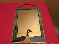 Full view of the stained glass mirror with blue-green border, Canadian goose and cattail motif at bottom left, and hanging chain.