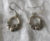 Front view of the pair of sterling silver Claddagh design earrings on fabric background.