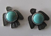Close front view of the pair of sterling silver thunderbird shaped stud earrings with turquoise stones, showing engraved feather details and central turquoise.
