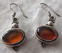 Close-up front view of vintage sterling silver earrings with oval amber cabochons capturing color and metal detail.