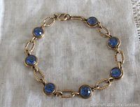 Vintage 12K gold filled link blue stone bracelet laid flat showing full length, blue faceted round stones with decorative gold filled links in good condition.