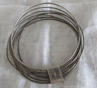 Top view of vintage sterling silver multi strand bangle bracelet showing 8 thin twisted and smooth strands joined by a flat loop with engraved star design.