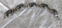 Full length view of the vintage sterling silver bracelet with five oval hematite stones in filigree settings on white fabric background.