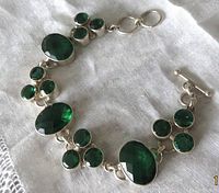 Full view of the sterling silver bracelet with multiple green facetted stones set in links and T bar clasp.