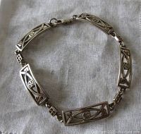 View of bracelet laid flat showing six rectangular openwork silver links and lobster clasp on white fabric background.