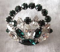 Front view of Sherman basket brooch with emerald green round stones and clear marquise stones prong set in rhodium plated metal.