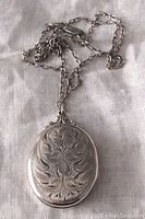 Photo showing front side of the sterling silver locket. Ornate floral engraving and decorative top detail visible.