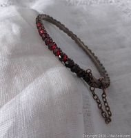 Side angled view of child-sized garnet bangle showing deep red stones and hinged metal clasp with safety chain attached.