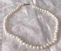 Full view of the pearl necklace laid flat on fabric showing the clasp and pearls.