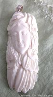 Front view of carved bone pendant showing goddess face, feathers, flower, and eagle beak details.