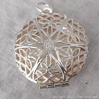 Top front view showing the round sterling silver locket pendant with pierced work floral pattern and attached bail.