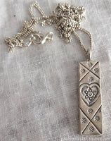 Photo of front side of rectangular sterling silver pendant on chain showing engraved heart and star floral design
