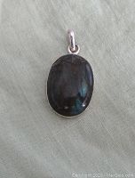 Oval labradorite pendant with sterling silver setting and bail, on a greenish fabric background, showing polished stone surface and silver hallmark.