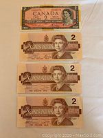 Four Canadian two dollar bills laid out on a surface: one older pink bill and three newer brown bills with Queen Elizabeth II portrait