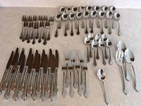 Full view of silverware spread out showing all pieces including forks, spoons, knives and serving utensils with ornate handle decoration.