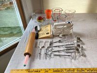 Full view of all kitchen items including mixer attachments, measuring cups, rolling pin, and cookie cutters on white tablecloth