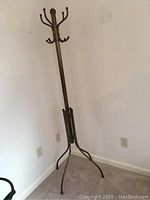 Full view of the tall brass coat rack tree stand with its tripod base and curved hooks at the top.