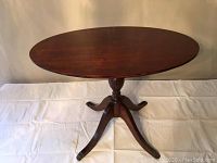Front diagonal view of the small wooden oval accent table showing the tabletop and pedestal base with three curved legs.