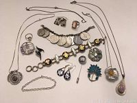 Full assortment of silver jewelry laid out on white surface including bracelets, rings, pendants, earrings, and chains.