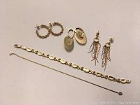 Five pieces arranged on white background: three pairs of earrings at top and two bracelets below