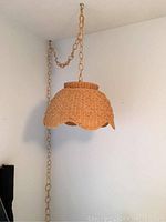 Wicker lamp hanging from ceiling with chain and cord showing scalloped edges of shade