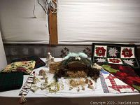 Overview of incomplete manger set with nativity figurines, Christmas-themed textiles and decor items spread out on a table.