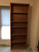 Full view of tall wooden bookcase showing overall size and six defined shelf spaces, wood grain visible on front edges.