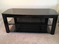 Front view of the TV stand showing dark tinted glass top and two lower glass shelves with metal mesh backing.