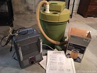Craftsman 8 gallon wet-dry shop vacuum with attached beige hose, Lakewood space heater, and boxed replacement cartridge filter on concrete floor.