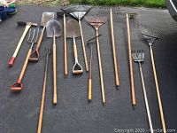 All nine long handled yard tools laid out on asphalt, showing full length and different tool heads.