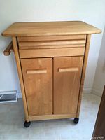 Front view of the wooden kitchen island cart showing drawer and cabinet doors on wheels.