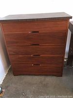 Front view of wooden chest of drawers showing five drawers with recessed handles and warm brown wood finish.