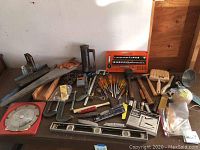 Wide view of the assortment of tools arranged on a table showing saws, hammers, screwdrivers, clamps, a level, and other tools.