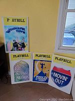 Four large colorful foam Playbill-style theater art signs leaning against wall, showing designs for Wonderful Town, The Sound of Music, Fiddler on the Roof, and Movin' Out