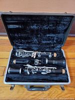 Photo showing black Bundy clarinet disassembled into upper joint, lower joint, barrel, bell, mouthpiece with ligature inside a hard carrying case with plush black lining.