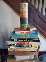 Stack of vintage board games and kits including a cylindrical tube game on top and various boxed games below.