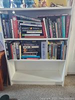 Front view of white wooden 3-shelf bookcase filled with books to show size and condition.