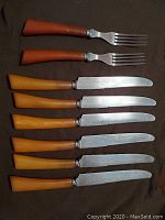 Set of six knives and two forks with bakelite handles in amber and brown tones, stainless steel blades and tines, laid out on dark fabric.