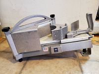 Side view of Nemco commercial tomato slicer on floor, showing handle, blade assembly, and base with stickers