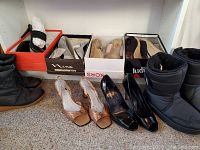 Full view of six pairs of women's shoes and boots in and out of boxes on shelf