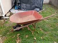 Full side view of a red metal wheelbarrow showing rust on tub and frame, with a black new tire.