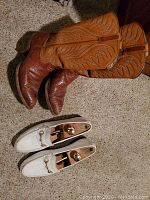 Photo of vintage cowboy boots in two-tone brown leather with decorative stitching next to white men's loafers with shoe stretchers inside