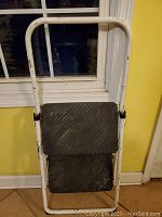 Front view of white metal stepstool with two black non-slip steps and curved support handle.