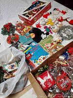 Photo showing full lot of vintage Christmas decorations including boxed Coca-Cola ornaments, assorted small cloth animal ornaments, vinyl records with illustrated holiday covers, and box with additional decorations in plastic bag.