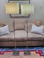 Two silver color floor lamps standing side by side with beige rectangular lampshades, showing full height and design.