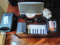 Overview of lot items including Bose speaker dock with power cord, Huawei smartphone in Roots case, hand roll-a-piano keyboard, black wallet, and white electronic device (likely the hand warmer).