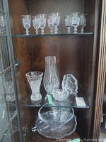 Middle shelf displaying 2 crystal vases (one tall cylindrical), crystal owl sculpture, crystal bowl, leaf-shaped serving plate, and small glass bowl.