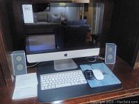 Wide front view of iMac with speakers, keyboard, mice and manuals on wood table