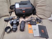 Full lot arranged on sofa: camera bag, camera with lens, second lens, hood, strap, charger, cables, manuals