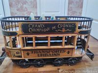 Side view of the wooden trolley showing hand-painted text 'FRANCE CHAMPAGNE DE COGNAC' and 'TRANSPORTS URBAINS' with black wheels and railings.